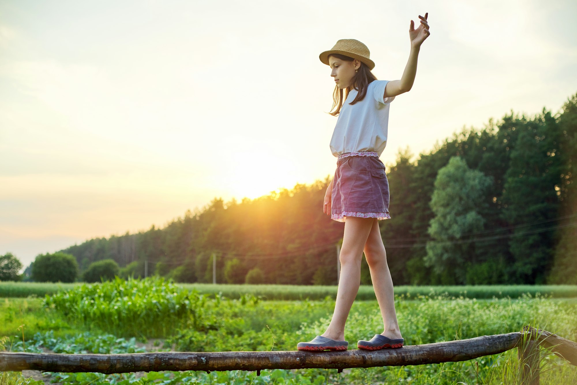 Summer, nature, happiness, childhood concept. Girl in hat walking on wooden fence